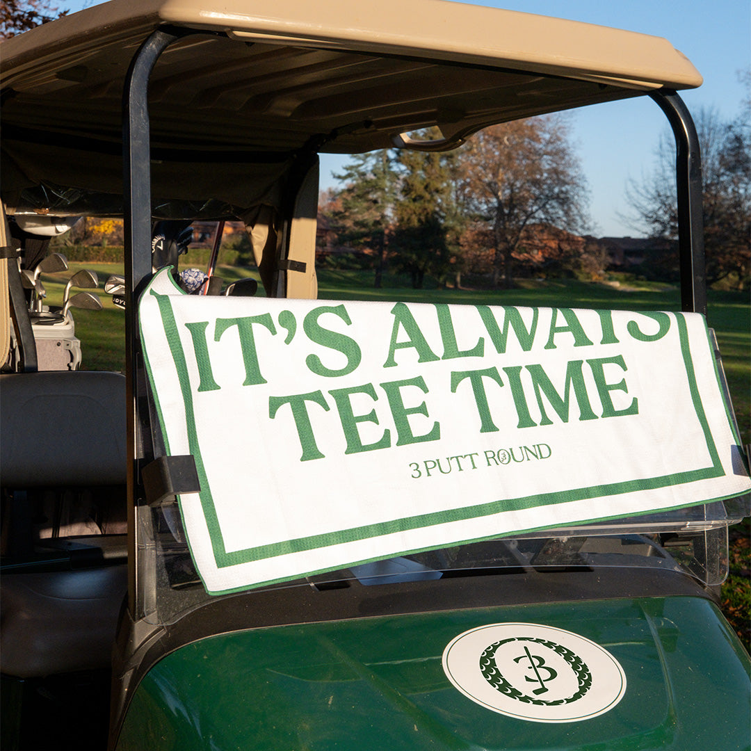Soft cotton golf towel by Three Putt Round featuring "It's Always Tee Time" print, with golf club and ball details in view.